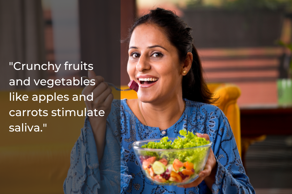 A woman sits indoors, smiling and holding a fork and a bowl of salad with lettuce, carrots, and cucumber. Text overlay discusses how crunchy fruits and vegetables can stimulate saliva and support good oral health.